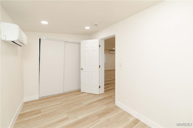 unfurnished bedroom featuring recessed lighting, baseboards, light wood-style floors, a closet, and a wall mounted air conditioner