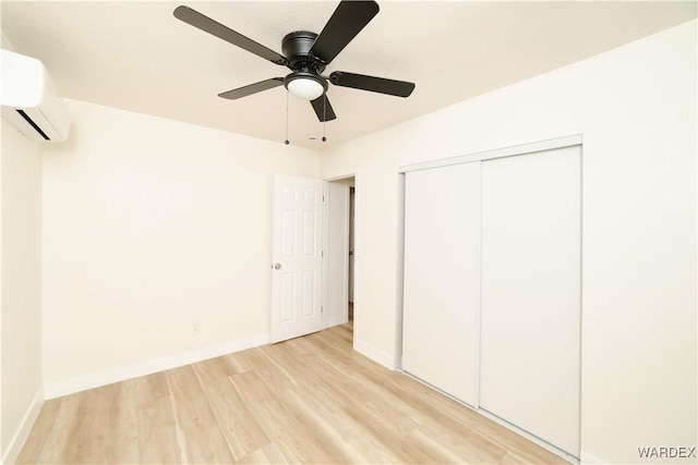 unfurnished bedroom with light wood-style floors, a closet, baseboards, and an AC wall unit