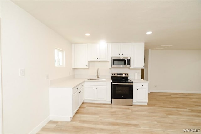 kitchen with light wood finished floors, light countertops, appliances with stainless steel finishes, white cabinetry, and a sink