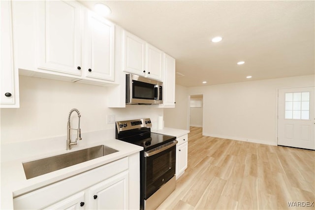 kitchen featuring appliances with stainless steel finishes, light countertops, light wood-style floors, white cabinetry, and a sink