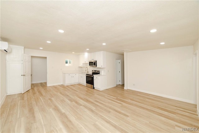 unfurnished living room featuring light wood finished floors, baseboards, a wall mounted air conditioner, a sink, and recessed lighting