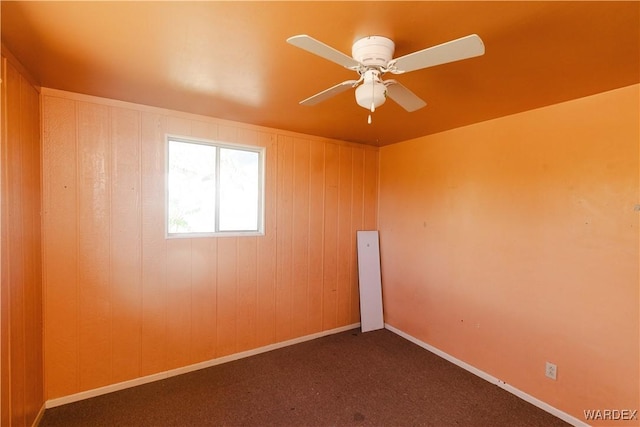 carpeted spare room featuring wood walls, baseboards, and a ceiling fan