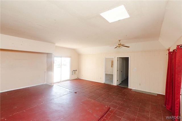 empty room featuring vaulted ceiling with skylight, a wall mounted AC, a ceiling fan, and wooden walls