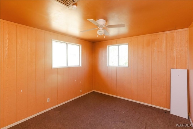 spare room featuring ceiling fan, dark colored carpet, plenty of natural light, and baseboards