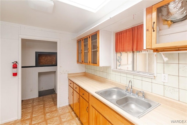 kitchen with a sink, light countertops, light floors, tasteful backsplash, and glass insert cabinets