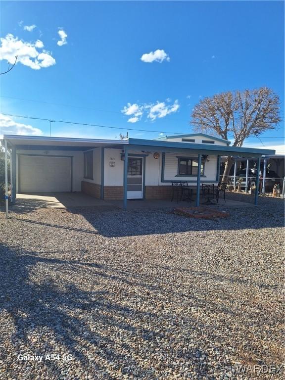 view of front of house featuring an attached garage, brick siding, gravel driveway, and an attached carport