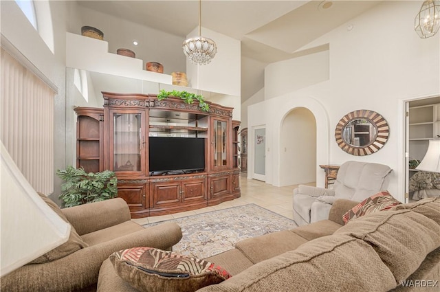 living room featuring arched walkways, light tile patterned floors, a towering ceiling, and an inviting chandelier