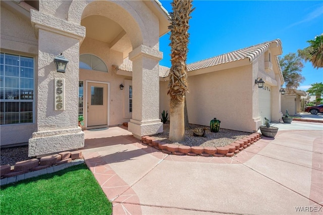 view of exterior entry with a garage, a tile roof, and stucco siding