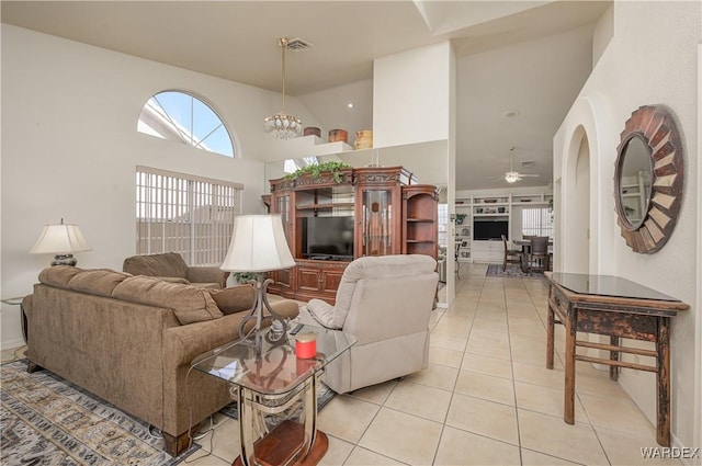 living area with light tile patterned floors, arched walkways, ceiling fan with notable chandelier, a high ceiling, and visible vents