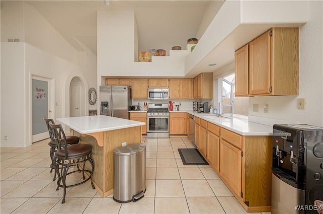 kitchen featuring light tile patterned floors, stainless steel appliances, a kitchen island, and a kitchen breakfast bar