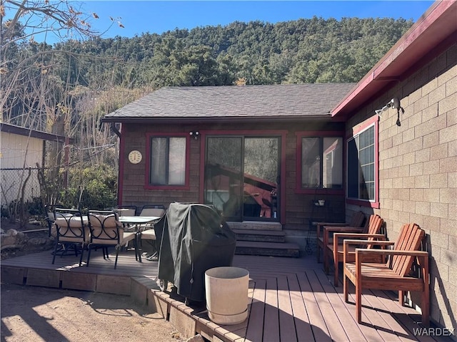 deck with a forest view, outdoor dining space, and grilling area