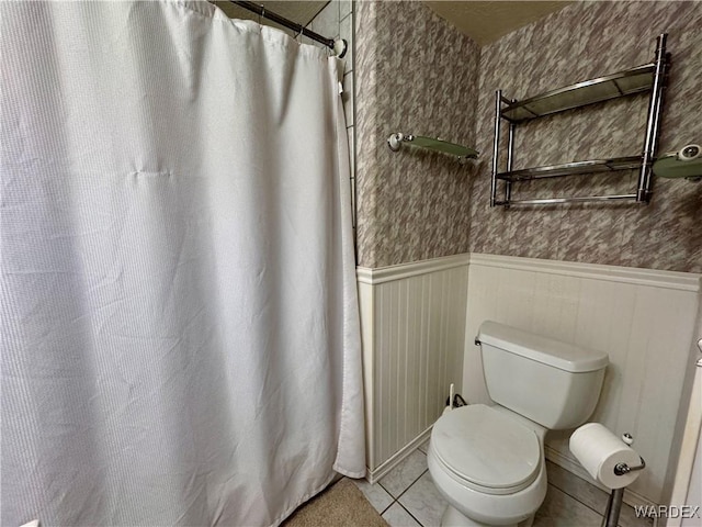 bathroom with curtained shower, toilet, wainscoting, tile patterned floors, and wallpapered walls