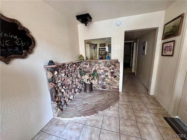 hallway with a textured wall, light tile patterned flooring, and visible vents