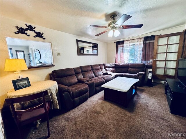 living area with ceiling fan, dark carpet, a textured ceiling, and a textured wall