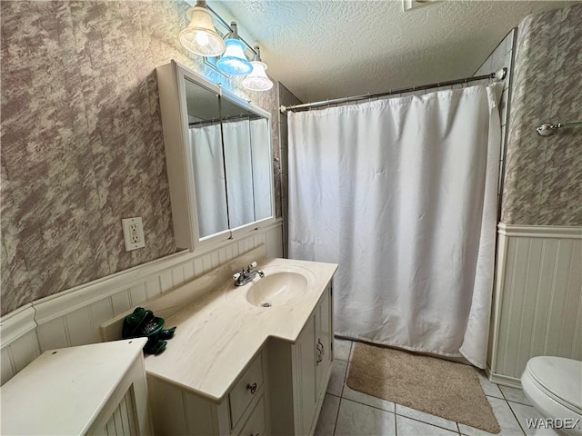 bathroom featuring a textured ceiling, tile patterned flooring, toilet, a wainscoted wall, and vanity