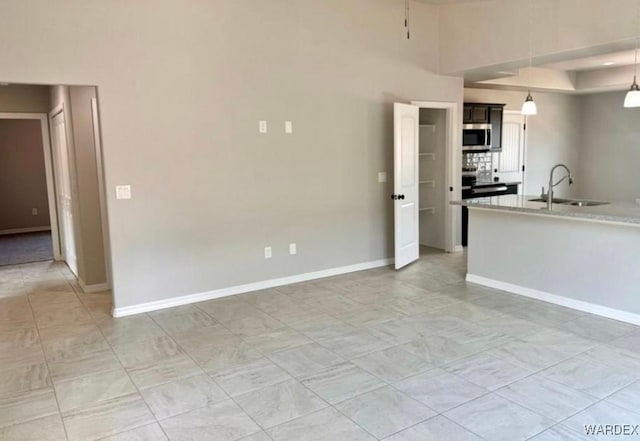 kitchen featuring decorative light fixtures, light countertops, stainless steel microwave, a sink, and baseboards