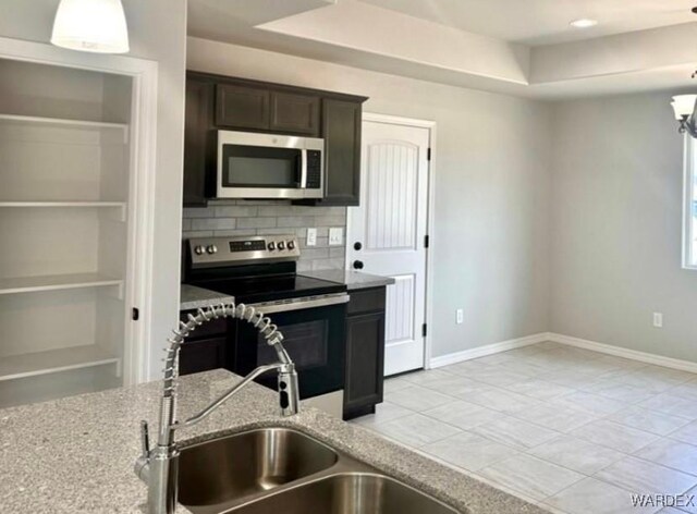 kitchen featuring dark brown cabinetry, tasteful backsplash, appliances with stainless steel finishes, light stone counters, and a sink