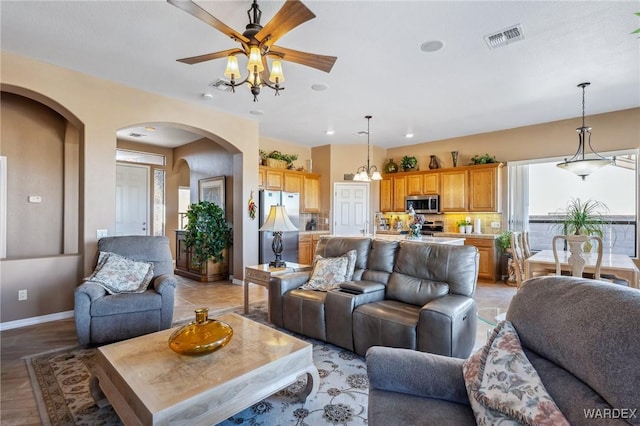 living area featuring ceiling fan, arched walkways, visible vents, and baseboards