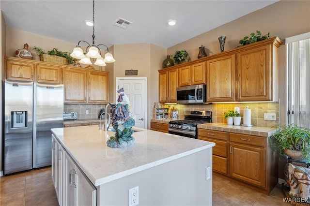 kitchen featuring pendant lighting, light tile patterned floors, visible vents, appliances with stainless steel finishes, and an island with sink