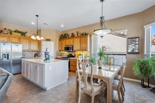 kitchen featuring stainless steel appliances, light countertops, a center island with sink, and hanging light fixtures