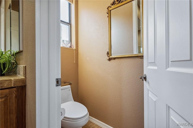 bathroom with a textured wall, toilet, and baseboards