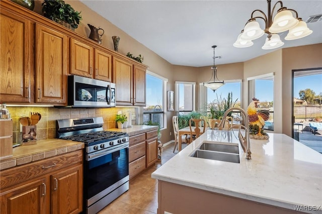 kitchen featuring appliances with stainless steel finishes, a sink, a center island with sink, and brown cabinets