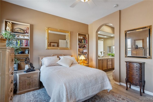 bedroom featuring arched walkways, light wood-style flooring, connected bathroom, ceiling fan, and baseboards