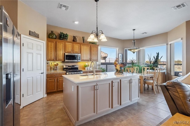 kitchen featuring visible vents, light countertops, appliances with stainless steel finishes, a center island with sink, and pendant lighting