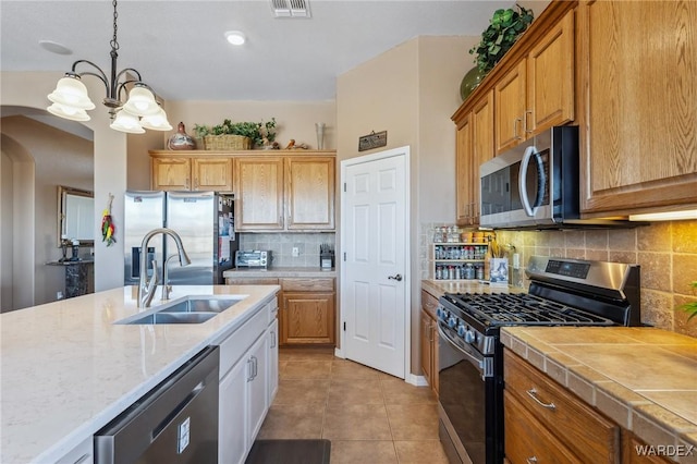 kitchen featuring light tile patterned floors, arched walkways, appliances with stainless steel finishes, hanging light fixtures, and a sink