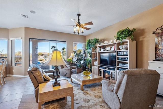 living area with a glass covered fireplace, visible vents, ceiling fan, and baseboards