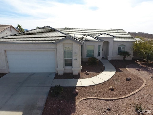 view of front of property featuring a garage, a tiled roof, concrete driveway, and stucco siding