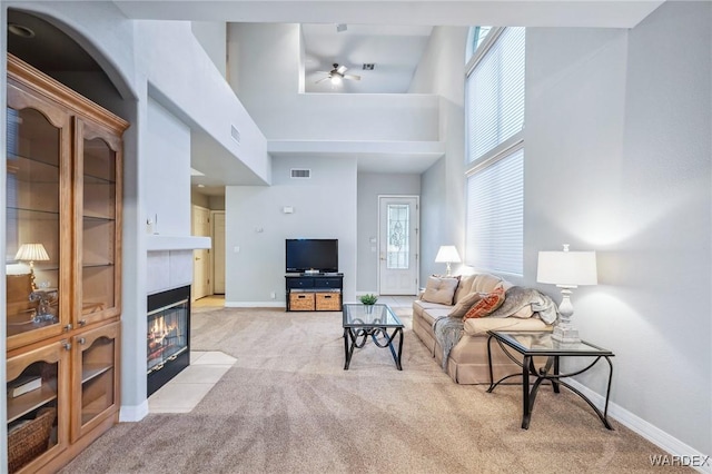 living room featuring light carpet, a towering ceiling, visible vents, baseboards, and a tiled fireplace