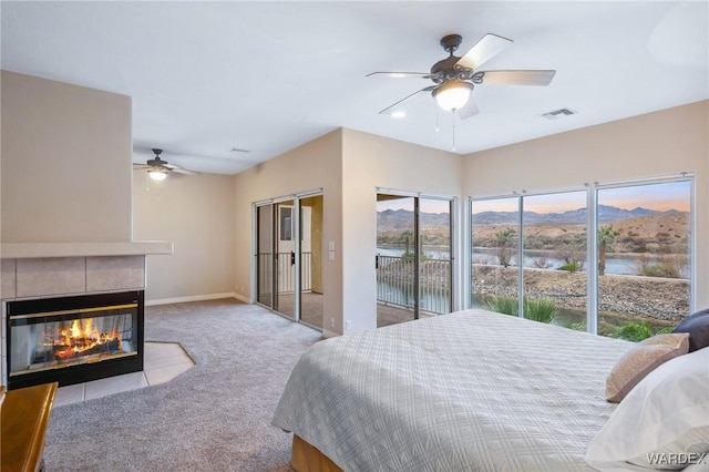 bedroom featuring access to exterior, light colored carpet, visible vents, a tiled fireplace, and a mountain view