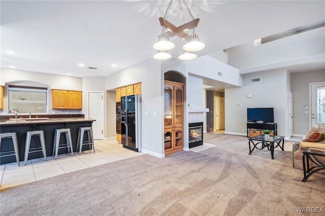 kitchen with light colored carpet, black fridge with ice dispenser, open floor plan, dark countertops, and a kitchen bar