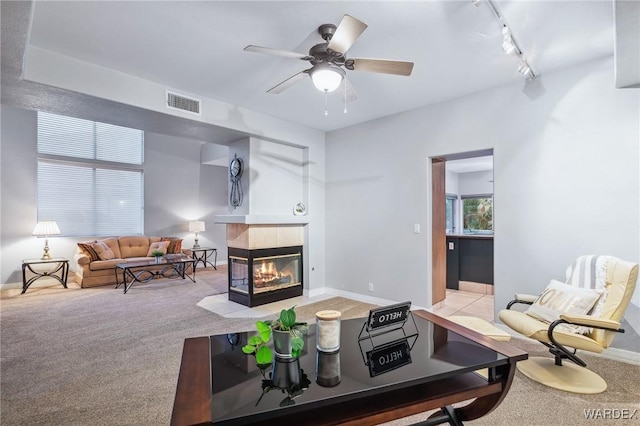 living area with ceiling fan, light colored carpet, visible vents, a tiled fireplace, and rail lighting