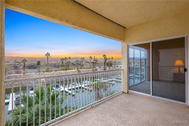 balcony at dusk featuring a water view