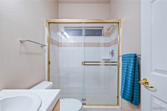 full bath featuring a textured wall, a shower stall, toilet, and vanity