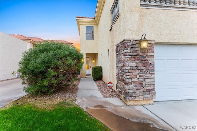 exterior entry at dusk featuring a garage, a tile roof, and stucco siding