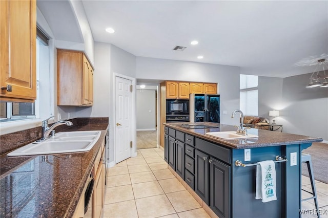 kitchen featuring visible vents, a center island with sink, a sink, and black appliances