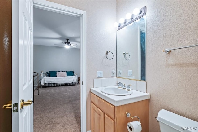 ensuite bathroom with a ceiling fan, a textured wall, toilet, ensuite bathroom, and vanity