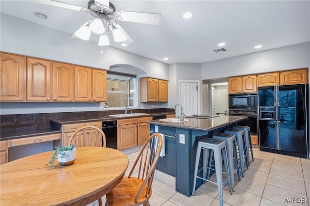 kitchen with visible vents, black appliances, a sink, and a center island with sink