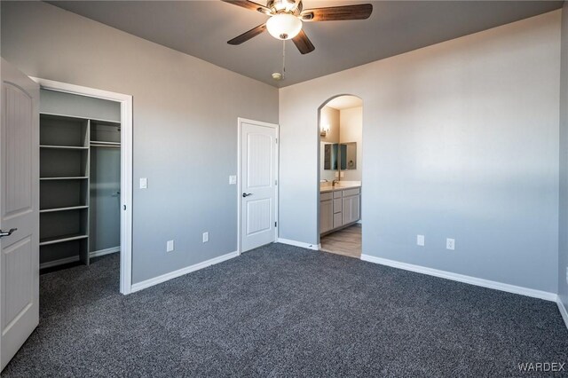 unfurnished bedroom featuring a walk in closet, baseboards, arched walkways, and dark colored carpet