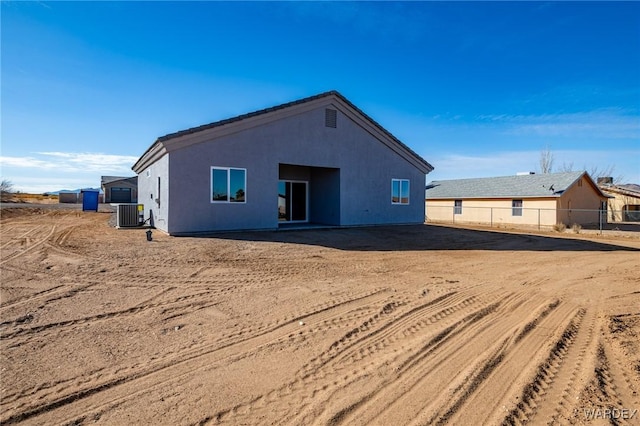 rear view of house with central air condition unit, fence, and stucco siding