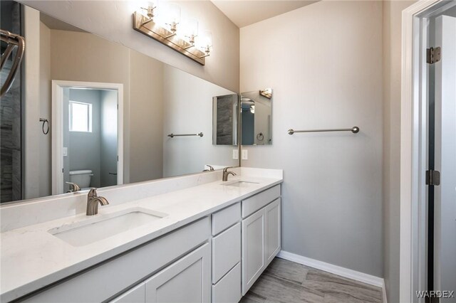 full bath featuring double vanity, a sink, toilet, and baseboards