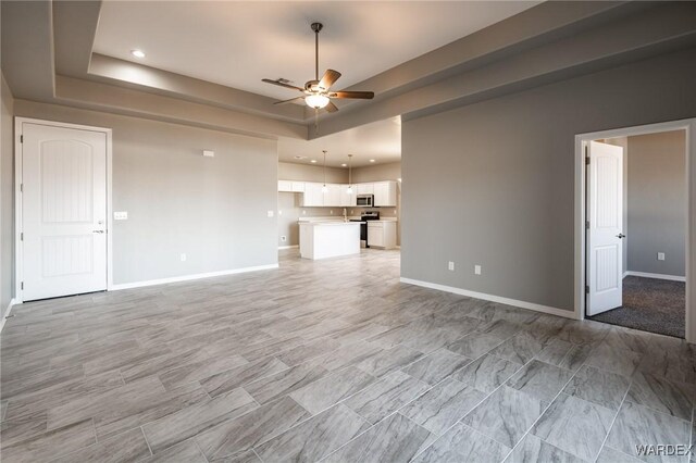 unfurnished living room with a tray ceiling, recessed lighting, a ceiling fan, and baseboards