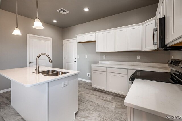 kitchen with stainless steel appliances, a sink, white cabinets, light countertops, and a center island with sink