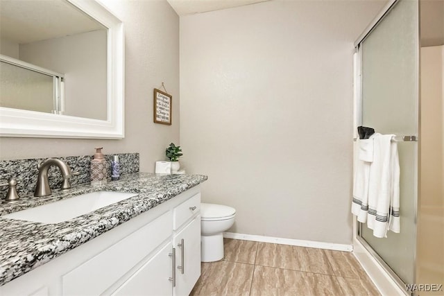 bathroom with toilet, a shower stall, baseboards, and vanity