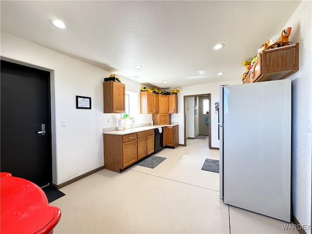 kitchen featuring baseboards, light countertops, black dishwasher, freestanding refrigerator, and brown cabinetry