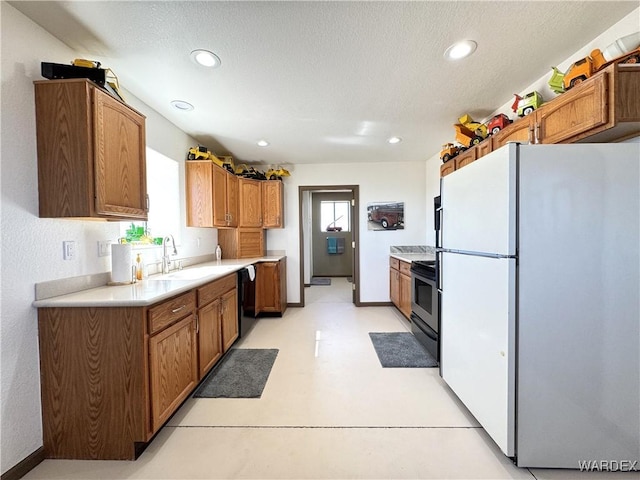 kitchen featuring stainless steel range with electric stovetop, a sink, freestanding refrigerator, light countertops, and dishwasher