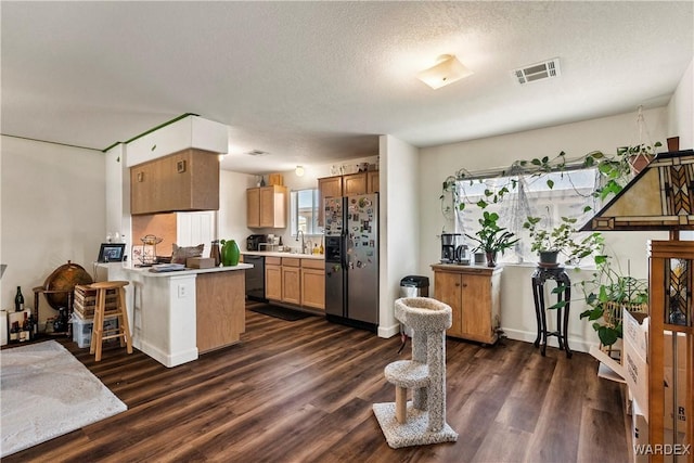 kitchen featuring black dishwasher, dark wood-style flooring, visible vents, stainless steel fridge, and a peninsula